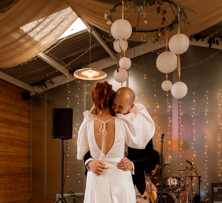 Bride in satin balloon sleeve 70s style wedding dress with open back design sharing the first dance with the groom at Hope Farm Dorset