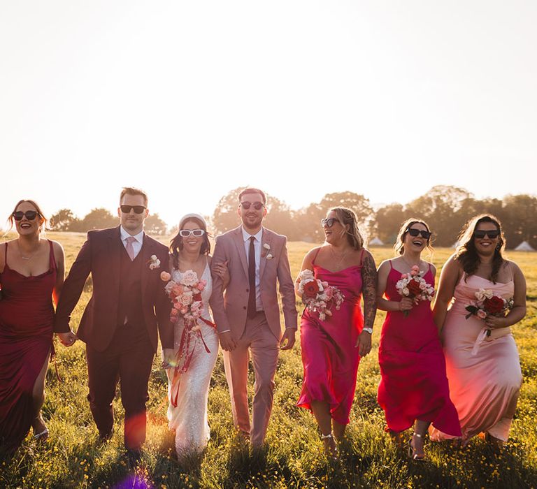 Golden hour wedding photo of the wedding party at sunset wearing different coloured pink bridesmaid dresses and suits 