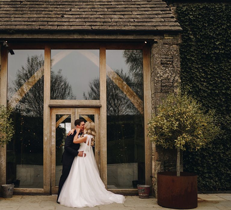 The bride and groom share a kiss at the entrance to their Stone Barn wedding venue 