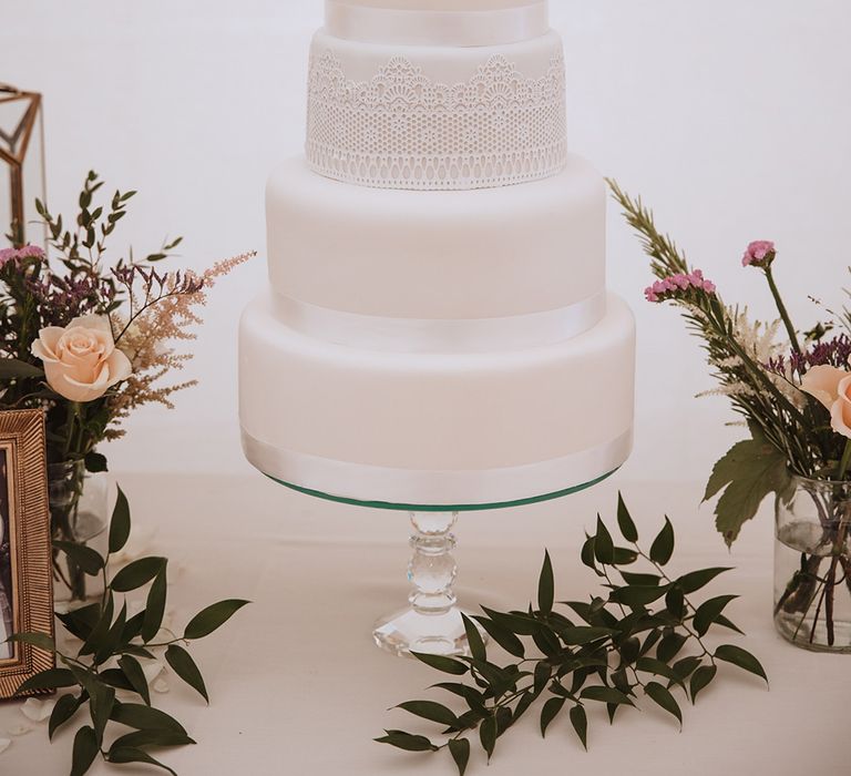 Four tier white iced traditional wedding cake with white ribbon and lace with pink flower decorations 