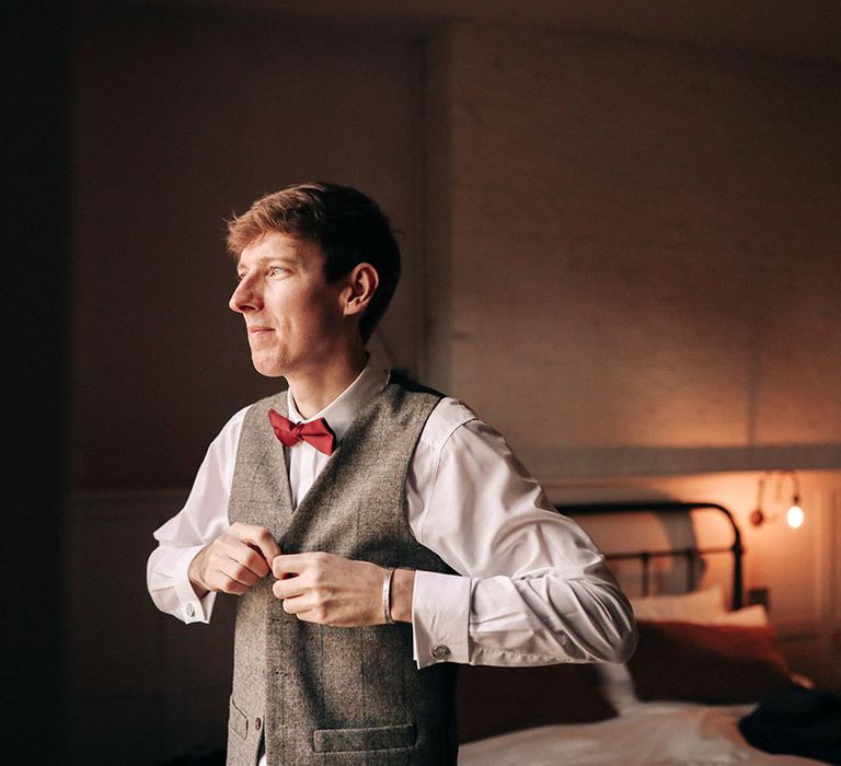 Groom wearing grey waistcoat with red bow tie getting ready for the wedding day