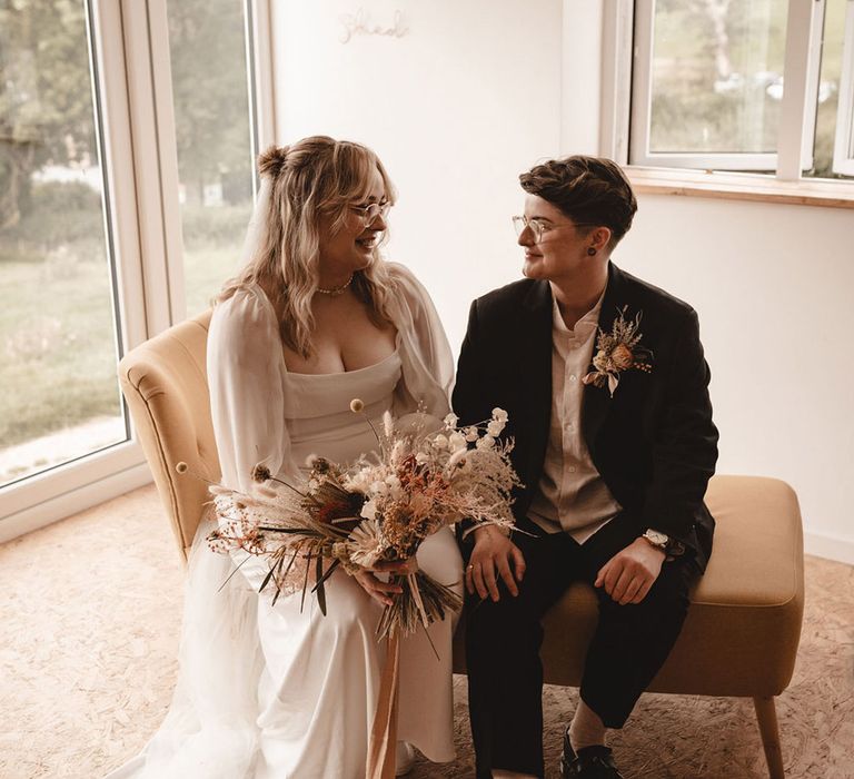 Bride wearing sheer long sleeve wedding dress with the bride in a brown suit for the lesbian wedding 