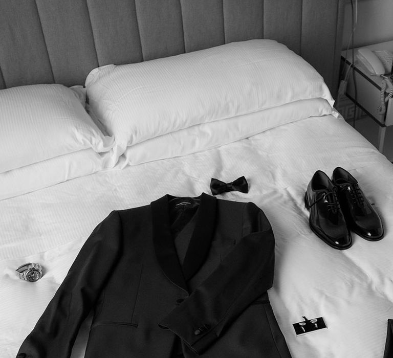 Groom's suit jacket, bow tie, cuff links and other accessories laid out 