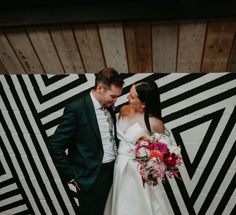 Groom in green suit with the bride in a strapless wedding dress carrying a pink wedding bouquet at industrial wedding venue 