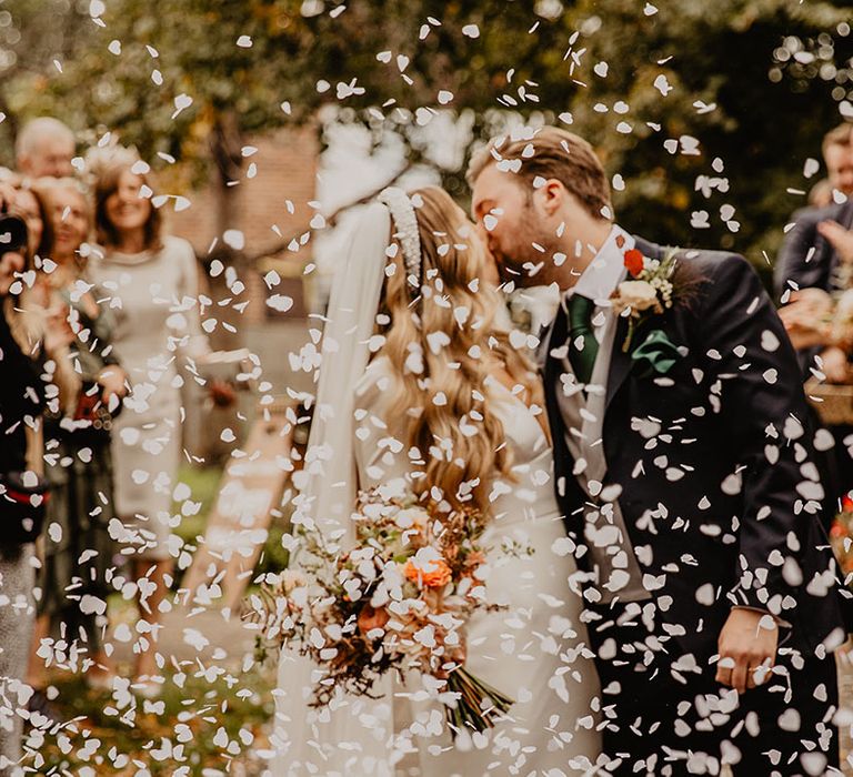 White confetti moment as the bride and groom share a kiss 