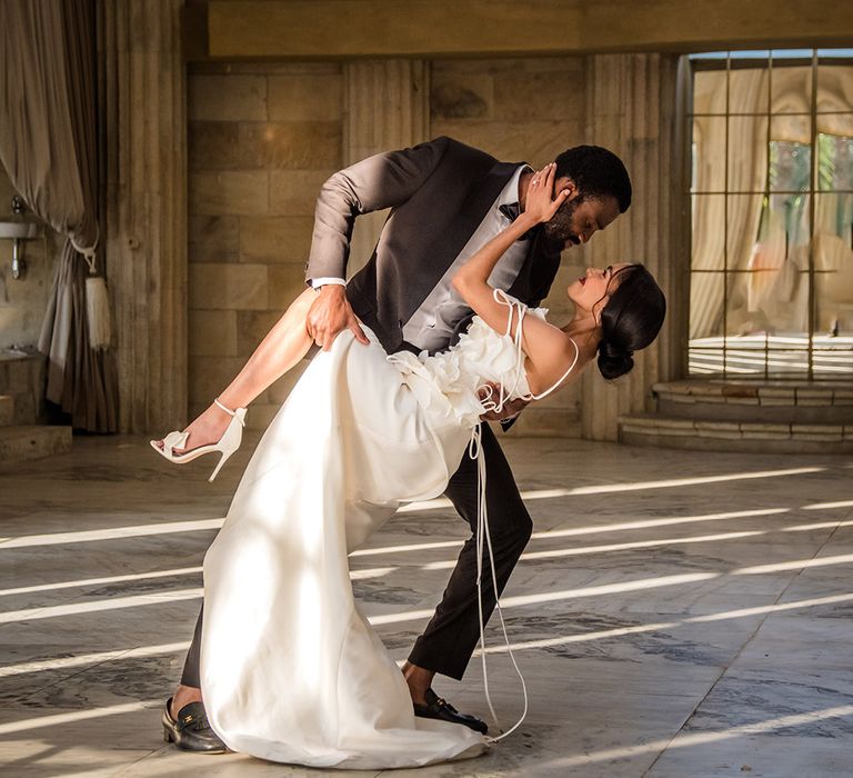 The groom in a black tuxedo sweeps the bride for a kiss who wears a 3D floral dress 