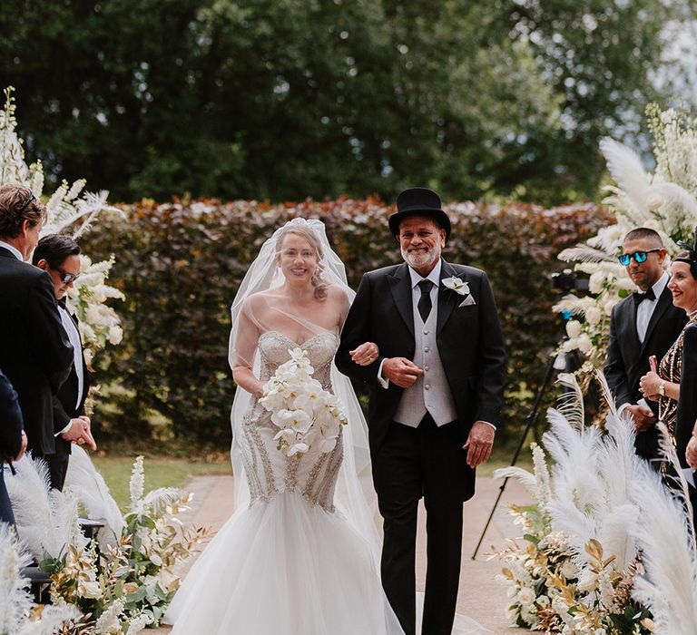 Father of the bride in top hat walking the bride down the aisle at their outdoor wedding ceremony 