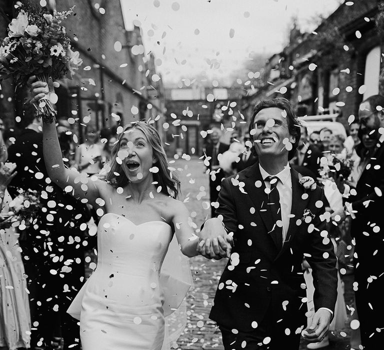 Black and white wedding photo of the bride and groom as confetti is thrown over them at city wedding in London 