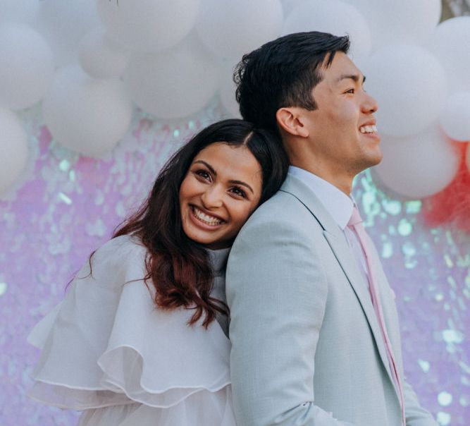 Bride in short wedding dress embracing her groom in pale green suit 