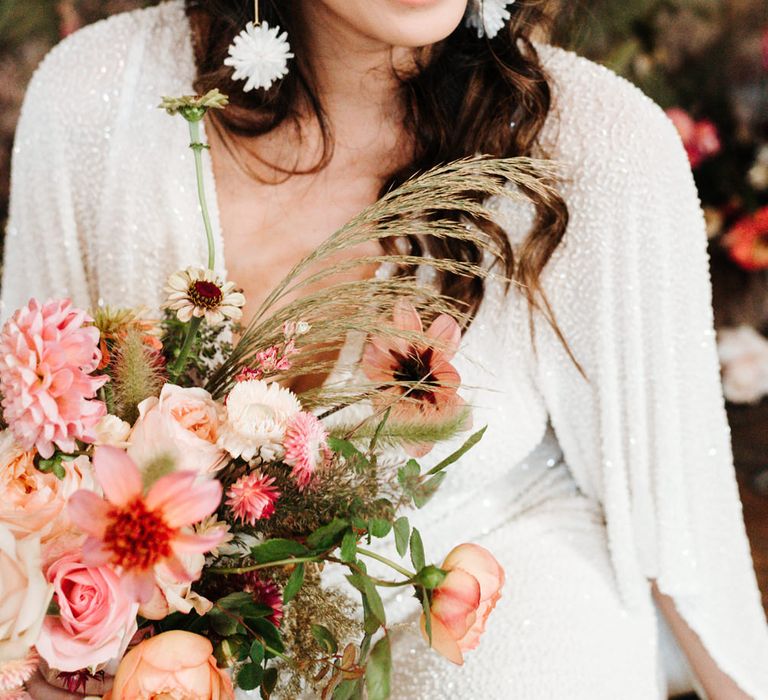 Beautiful bride with long earrings holding a colourful bouquet 