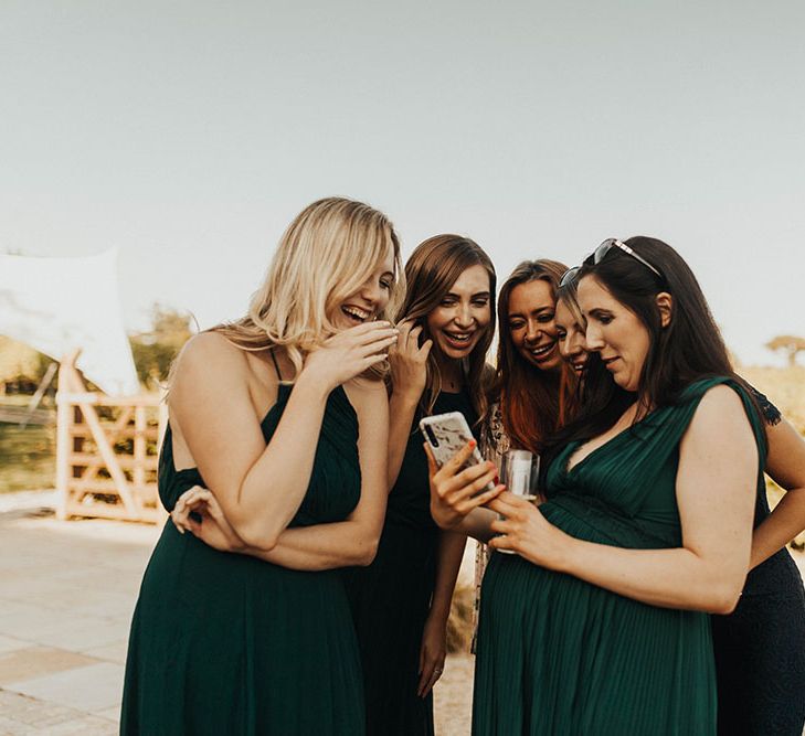 Bridesmaids huddle over a mobile phone in deep green dresses