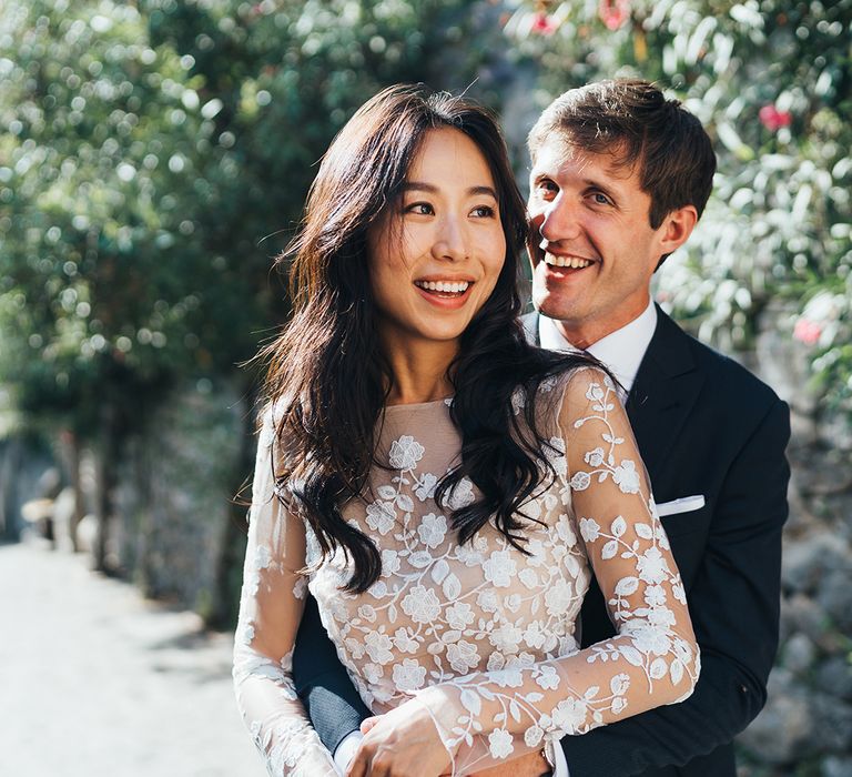 Groom embracing his bride in an appliqué jumpsuit with long sleeves 