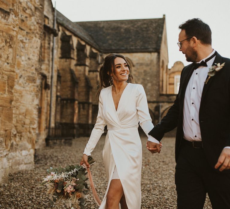 Bride & groom walk together holding hands on wedding day 