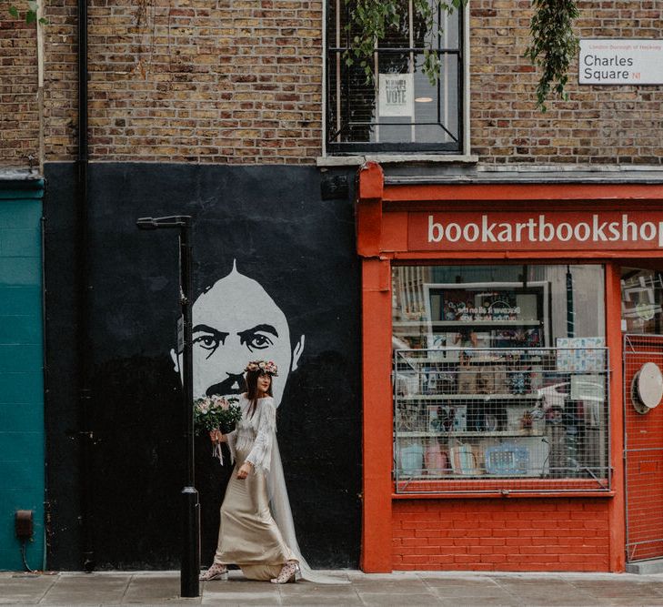 Bride walking down street holding protea bouquet and passing portrait on wall