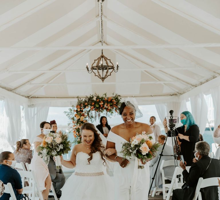 Black bride in a wedding jumpsuit and bi-racial bride in a strapless wedding dress descending down the aisle as wife and wife 