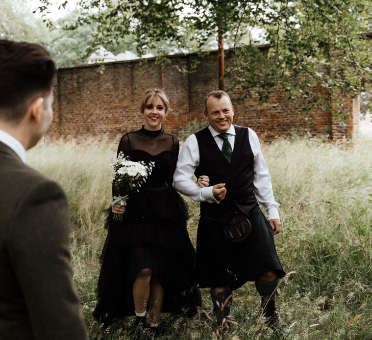 Bride walks through woodlands to groom during wedding ceremony