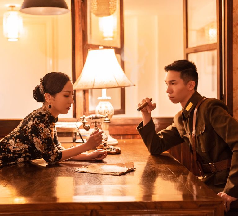 Bride-to-be looks across the table at her partner with light behind them 