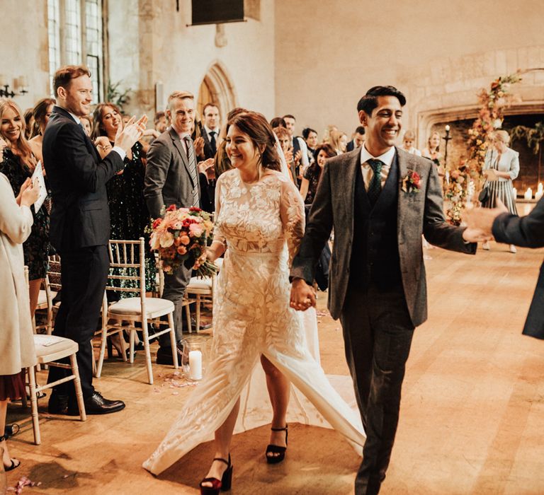 Bride and groom descending up the aisle as husband and wife in a lace Hermione De Paula wedding dress with front split and grey wool suit 