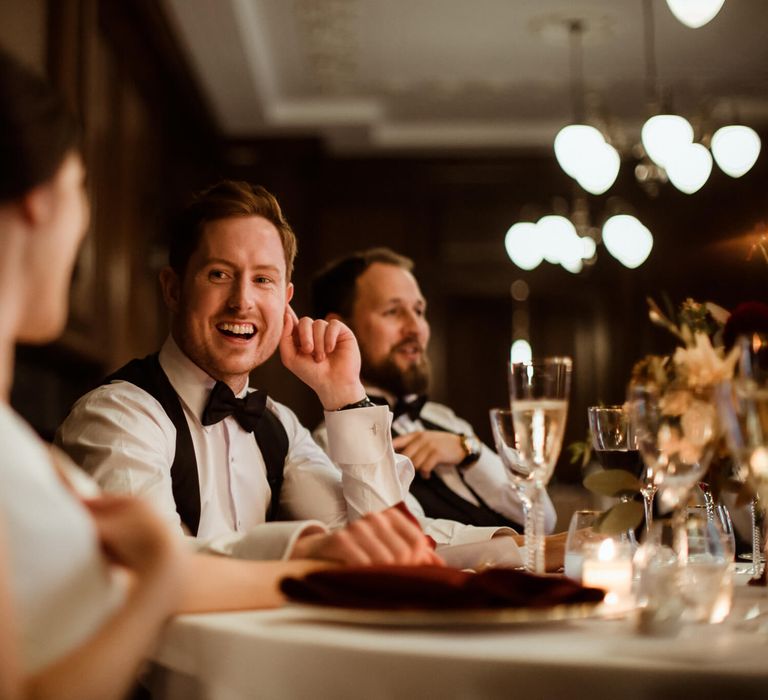 Groom laughing looking at his wife at the wedding breakfast table 