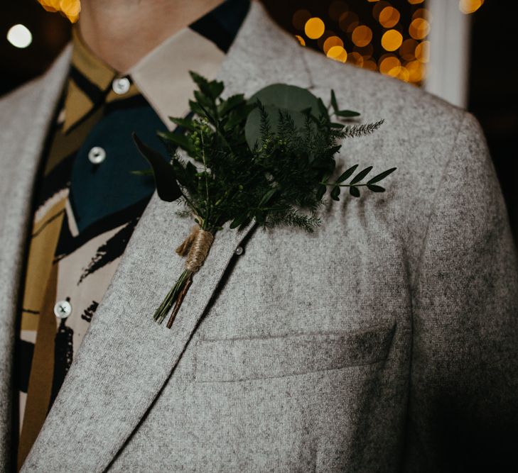 Groom in a grey suit and patterned shirt wearing a green foliage buttonhole