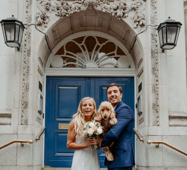 Bride & groom pose with their dog outside wedding venue