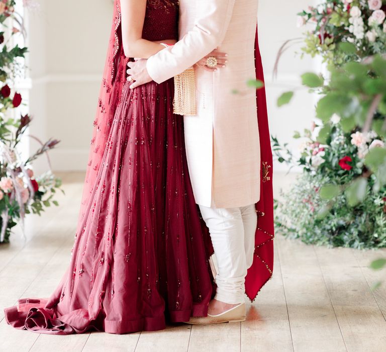 Bride & groom embrace on their wedding day under floral archway 