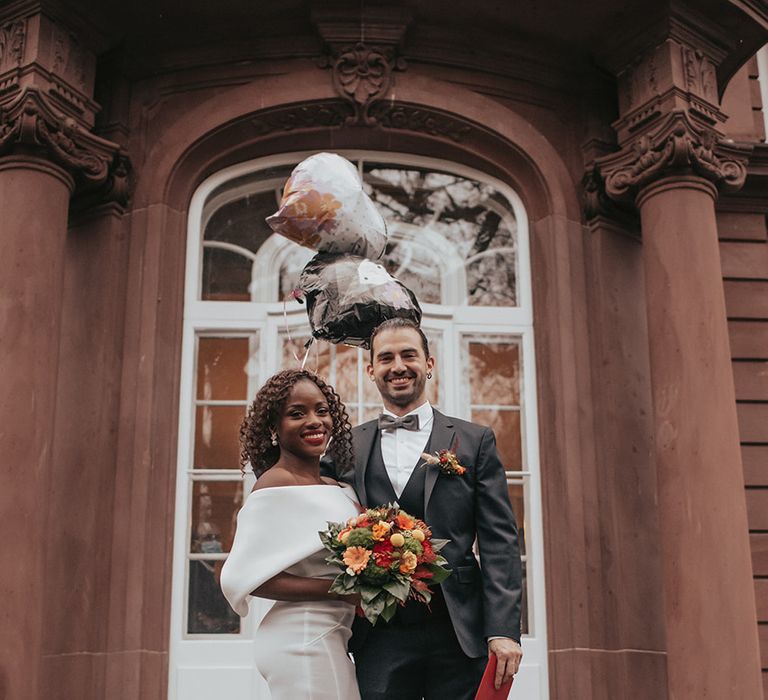 Bride & groom stand on the stairs with heart shaped balloons after marrying