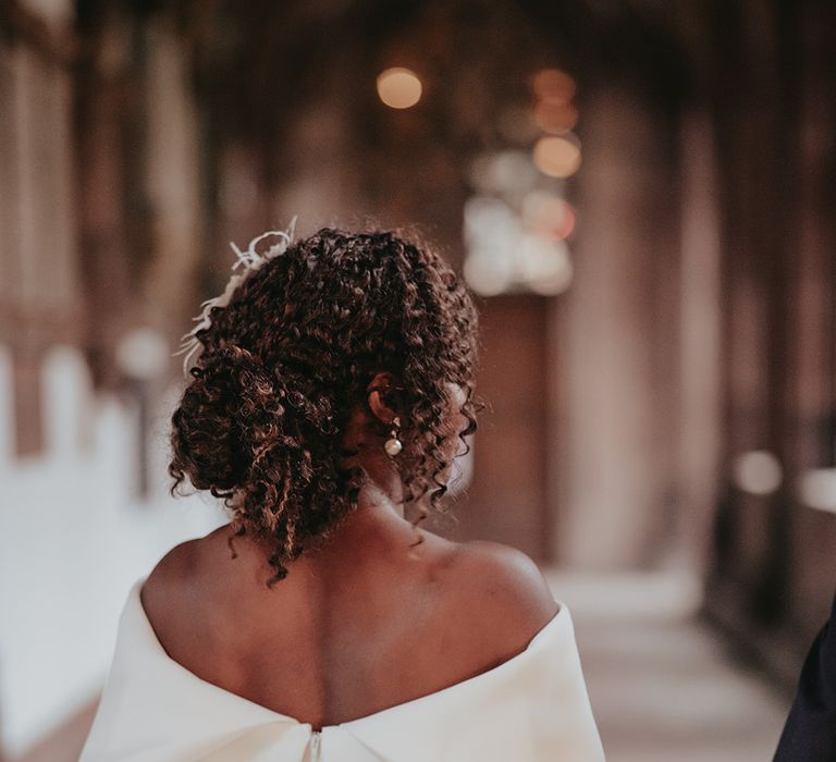 Black bride wears off the shoulder wedding gown whilst walking away with back turned to camera