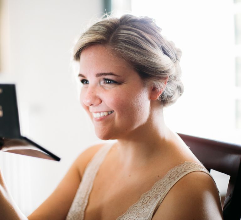 The bride smiling and looking into the mirror on her makeup palette