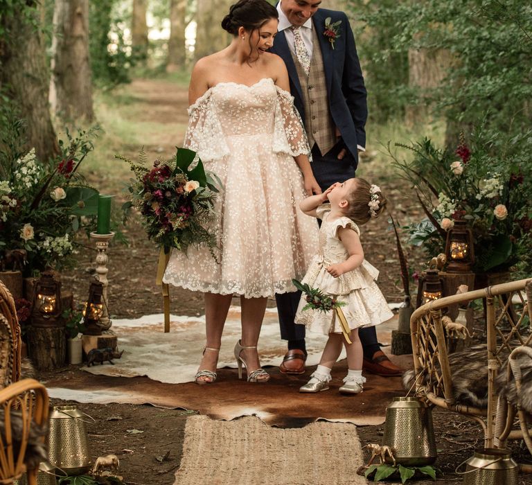 Bride & groom stand under trees with little girl surrounded by lights