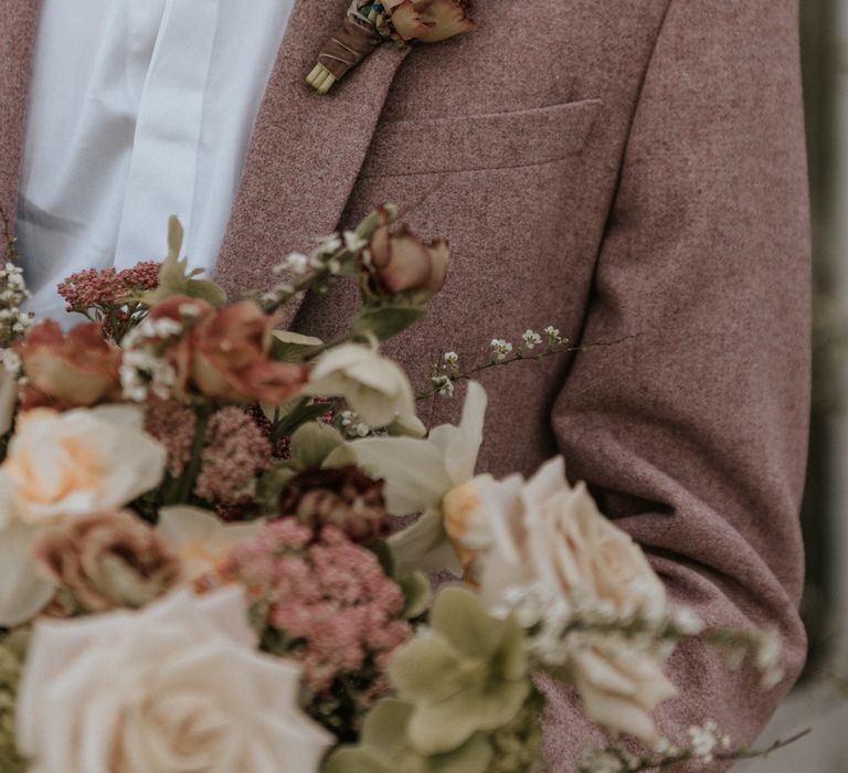 Groom wears pastel pink suit with white shirt and pastel blue floral buttonhole 