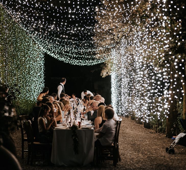 Twinkling blanket of fairy lights above outdoor wedding reception during the night 