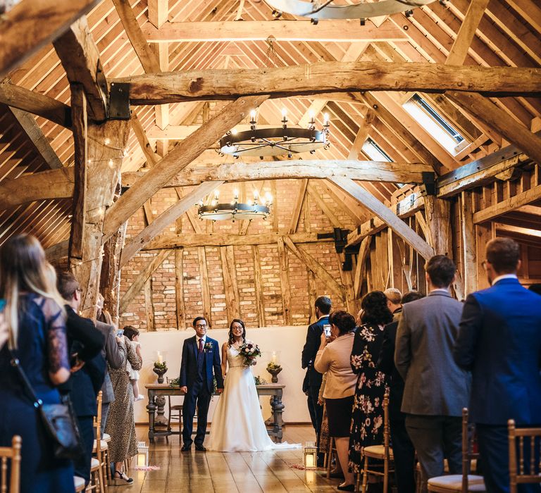 Bride & groom stand at the front of barn on the day of their wedding during ceremony