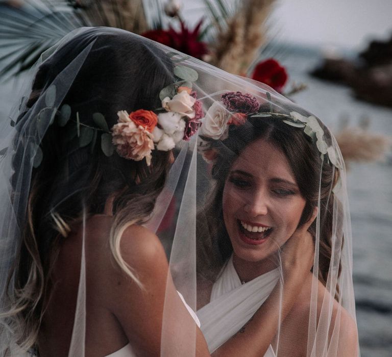 Two brides laughing and hugging under one large veil