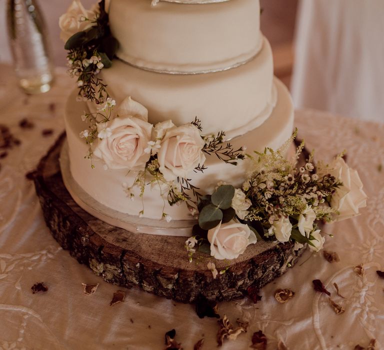 Four tiered white wedding cake with white icing and rose and white flower decor at home farm wedding