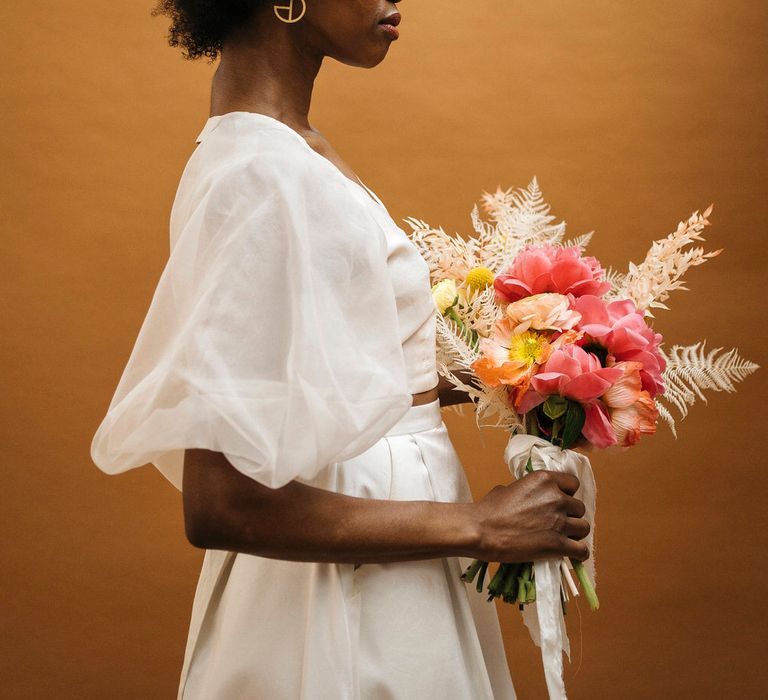 Bride wearing fresh flowers in her afro, carrying a matching bouquet and wearing a puff sleeve wedding top