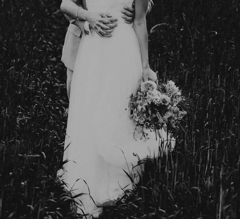 Groom embraces bride from behind for black & white photo as she laughs and smiles