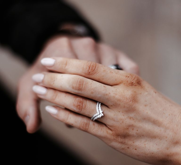 Bride & groom hold hands as bride wears V shaped wedding rings and neutral coloured nails