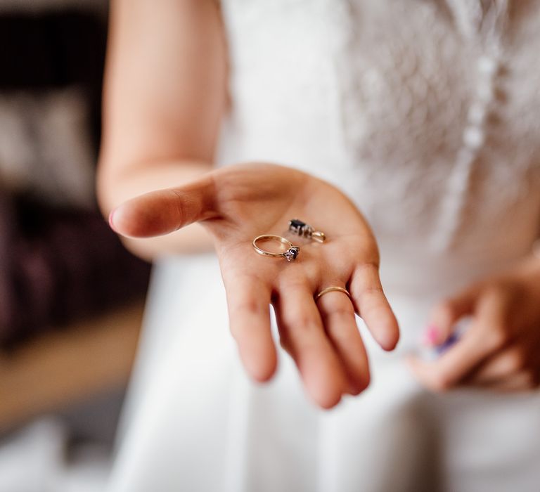 Bride in white lace button detail wedding dress holds out silver ring with blue gemstone before wedding at The West Mill Derby