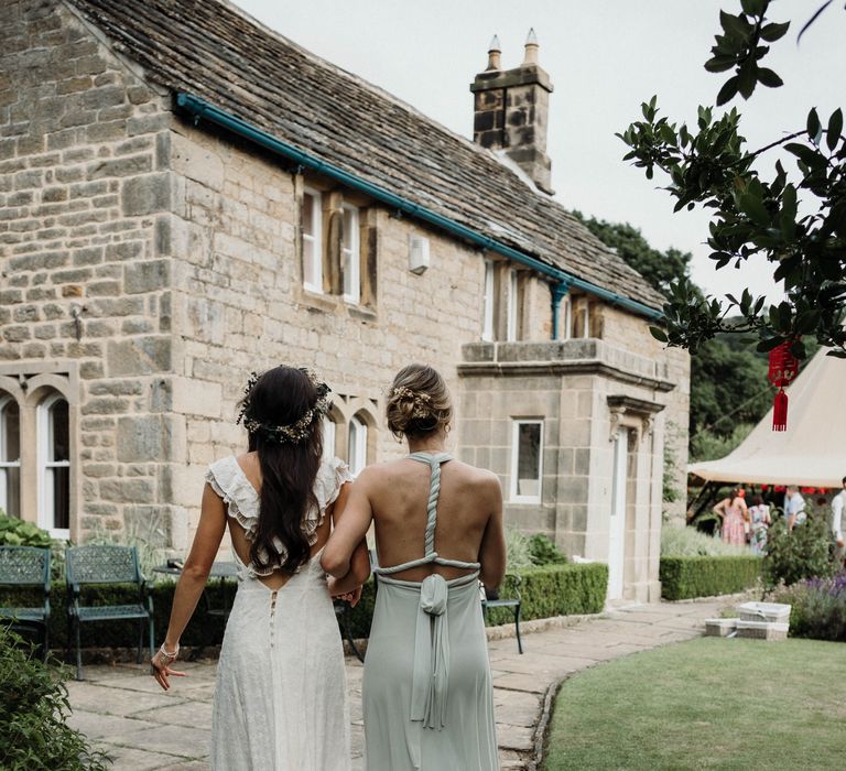 Bridesmaid wraps her arm around bride as they walk together