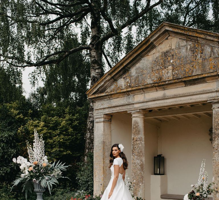 Bride in a taffeta strapless princess wedding dress with cape detail in the gardens at Barnsley House