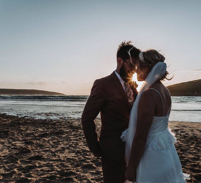 Bride & groom look lovingly at one another on the beach as the sun sets behind them