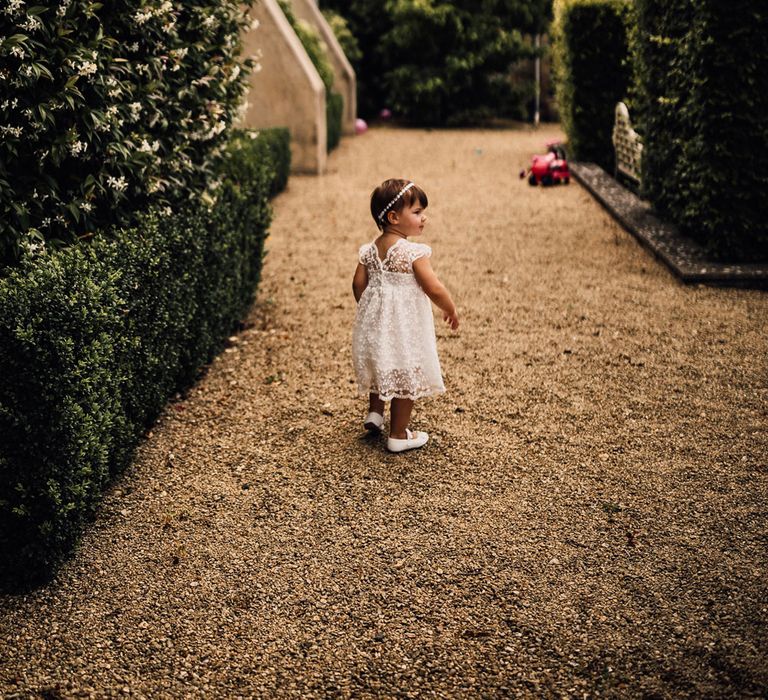 Flower girl in lace dress with cap sleeves walks down outdoor aisle as guests watch on for outdoor wedding ceremony in Dorset with pampas grass decor