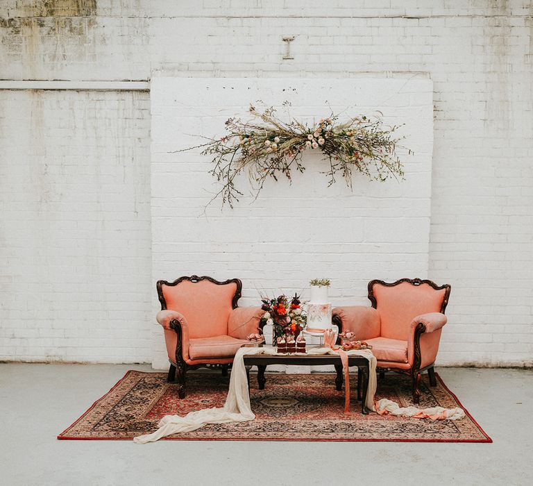 Hanging floral installation above a dessert table seating area with terracotta chairs, illustrated wedding cake and glazed doughnuts 