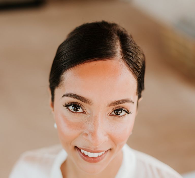 Bride smiles at the camera as she has her makeup done on the morning of her wedding day | Hannah MacGregor Photo & Film