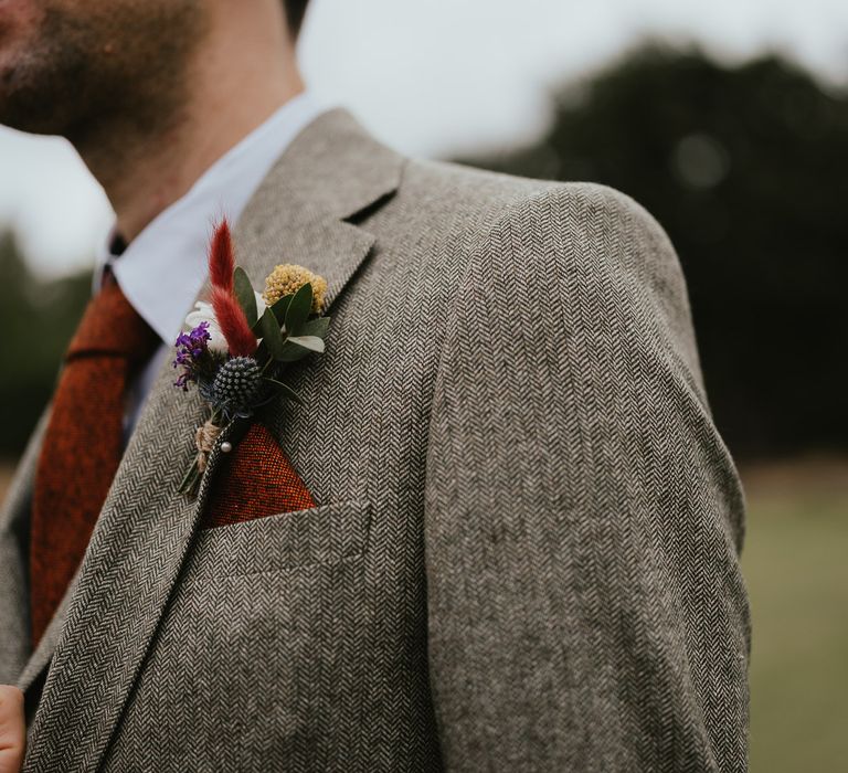 Groom in grey three piece herringbone suit, red tie and pocket square and floral buttonhole before late summer wedding in Norfolk