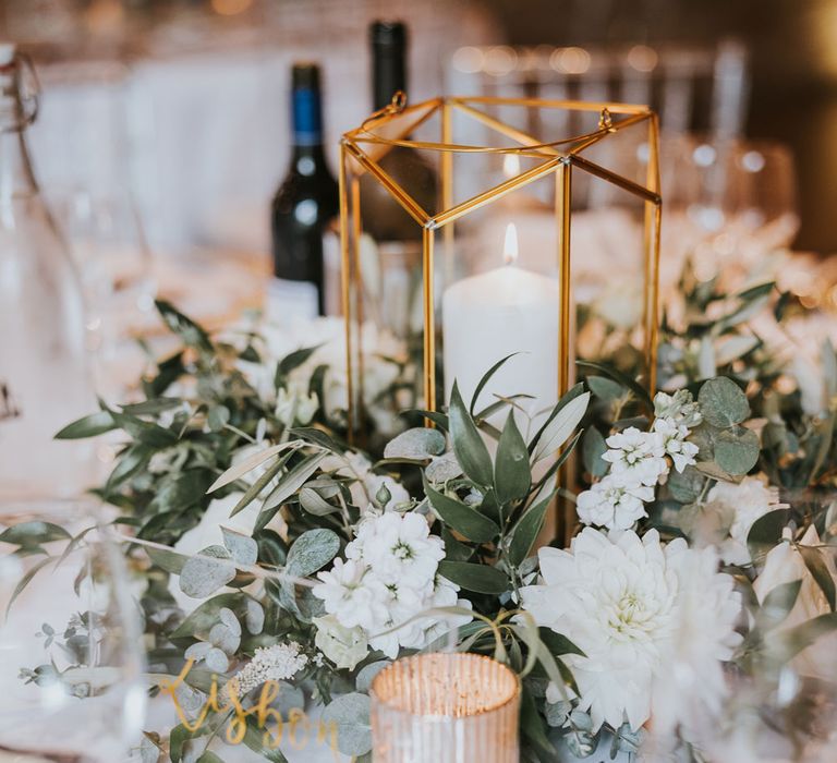 White and green floral centrepiece with candle in glass holder for elegant wedding table at Notley Abbey