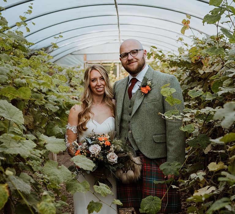 Bride & groom stand surrounded by foliage on their wedding day