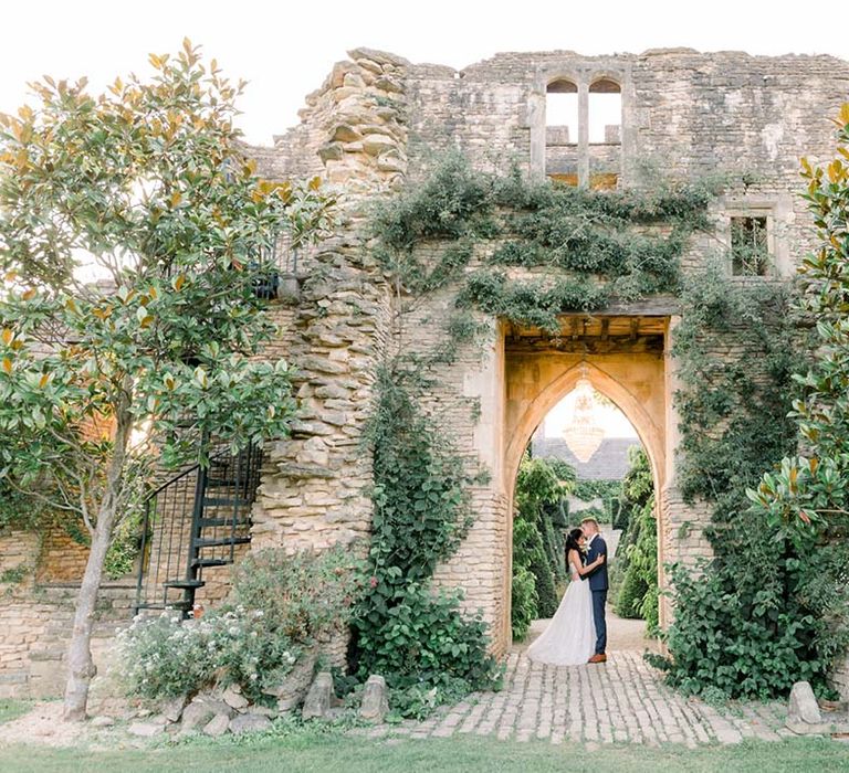 Bride & groom kiss under archway outdoors on their wedding day