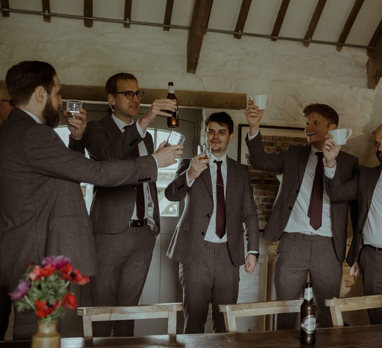 Groom stands with his groomsmen who wear brown suits 